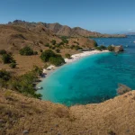 Tropical beach and turquoise bay surrounded by dry hills and anchored boats in Komodo